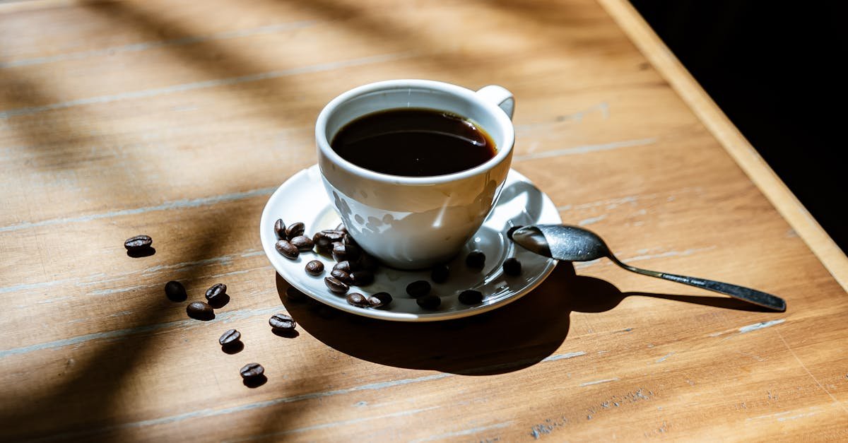 A sunlit coffee cup with scattered beans on a wooden table creates a warm, inviting still life scene.